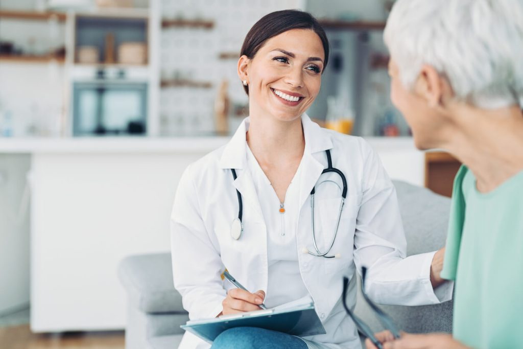 Eine freundliche Ärztin spricht mit einer älteren Patientin und lächelt